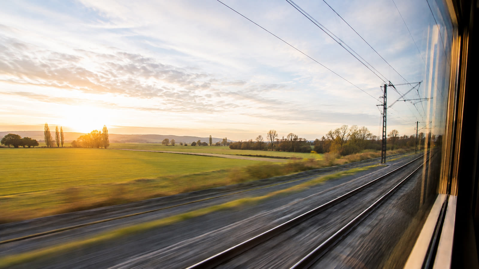 La voie ferroviaire à contre-jour du soleil couchant, vue depuis la fenêtre d'un train en marche.